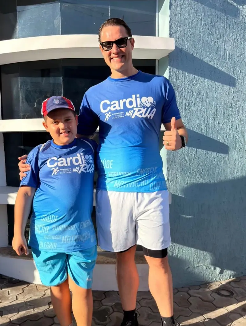 O Dr. Michel, de camisa azul do Cardio na Rua, faz sinal de positivo abraçado a um menino com a mesma camisa.