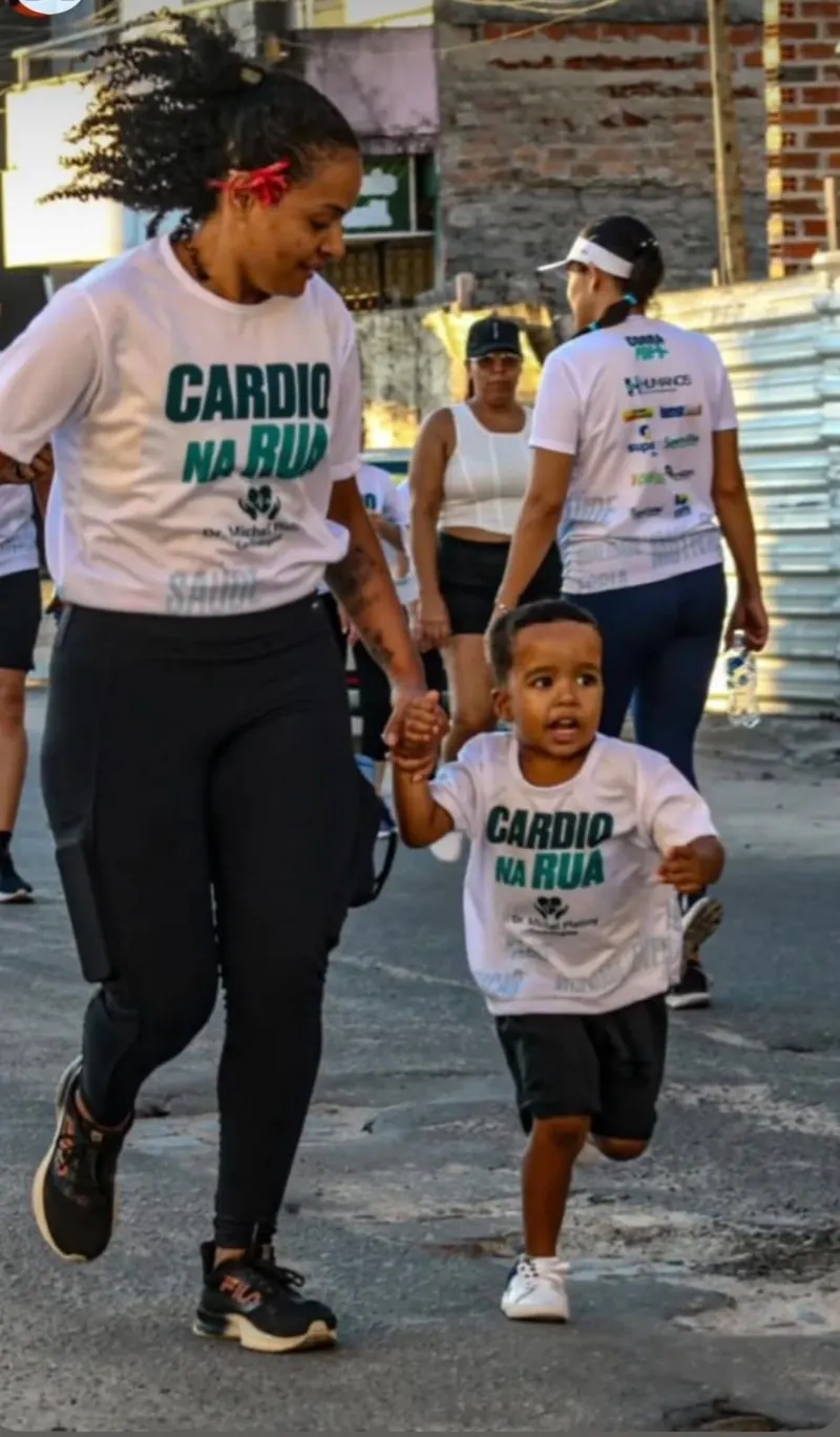 Mãe e filho pequeno, de mãos dadas, correm com a camisa do Cardio na Rua.