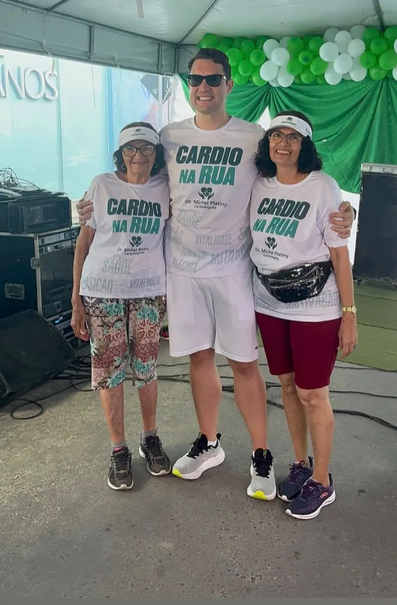 O Dr. Michel entre duas participantes, de camisa e viseira do evento, na tenda do Cardio na Rua.