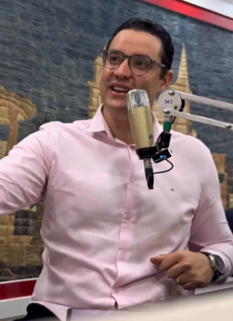 O Dr. Michel gesticula enquanto fala ao microfone no estúdio.